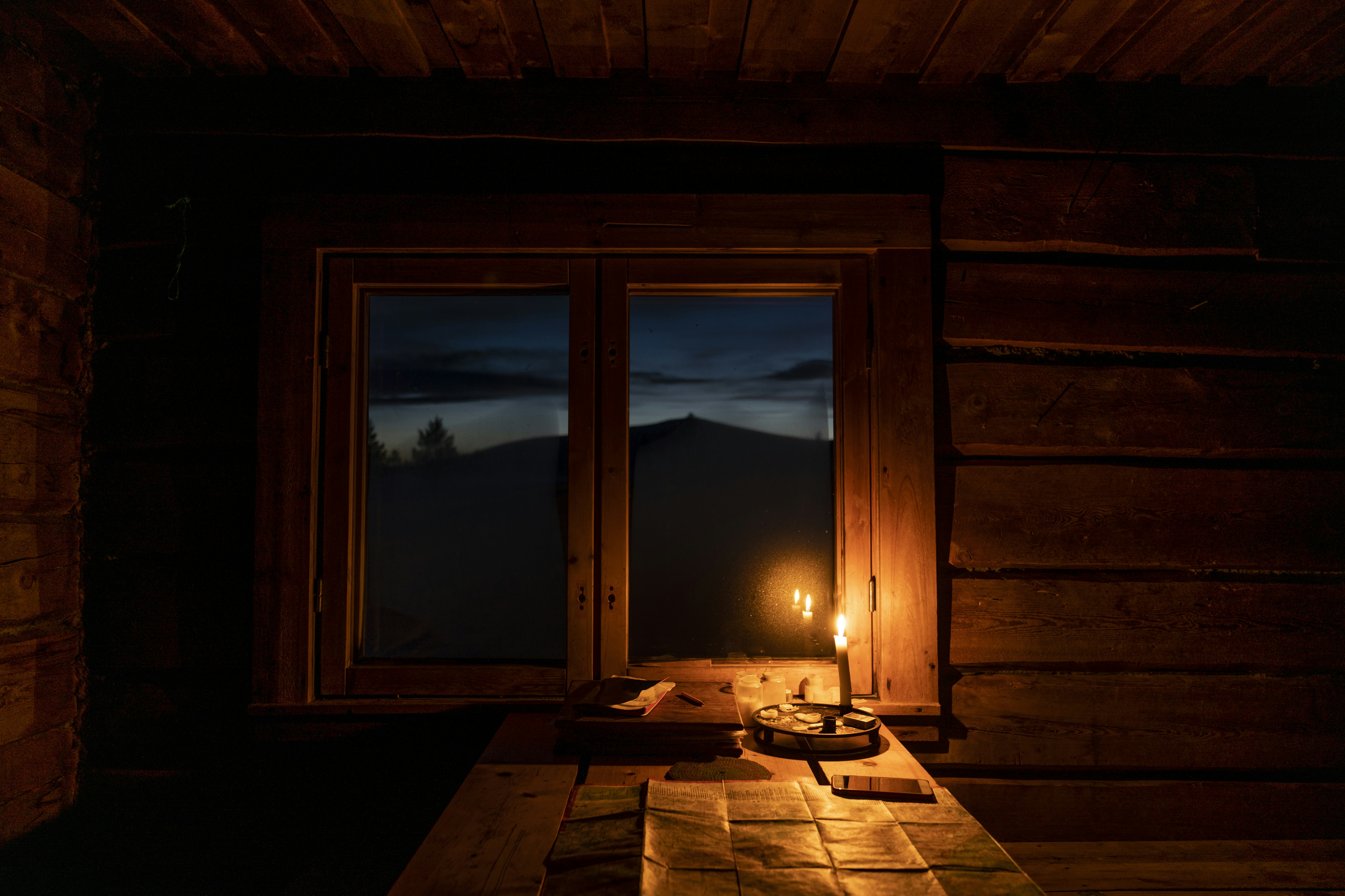 a candle is lit on a table in a cabin, Studying the map in the cabin while night falls.