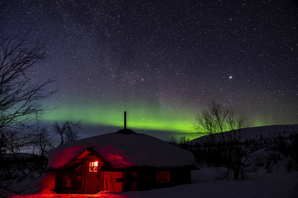une cabane dans la neige avec une lumière d’aurore verte et rouge en arrière-plan