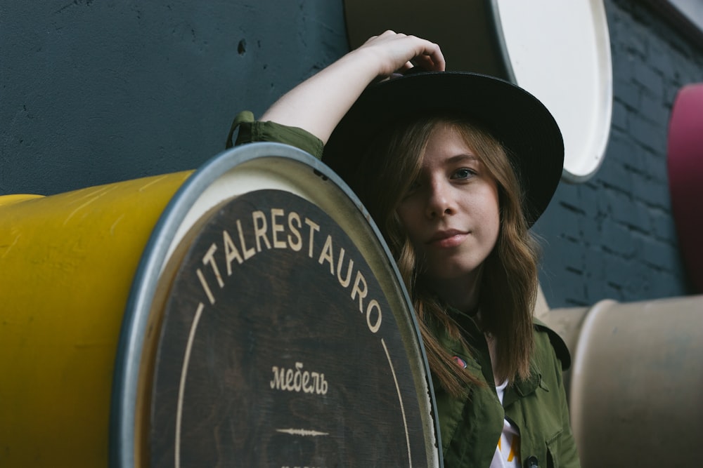 a woman wearing a hat leaning against a barrel