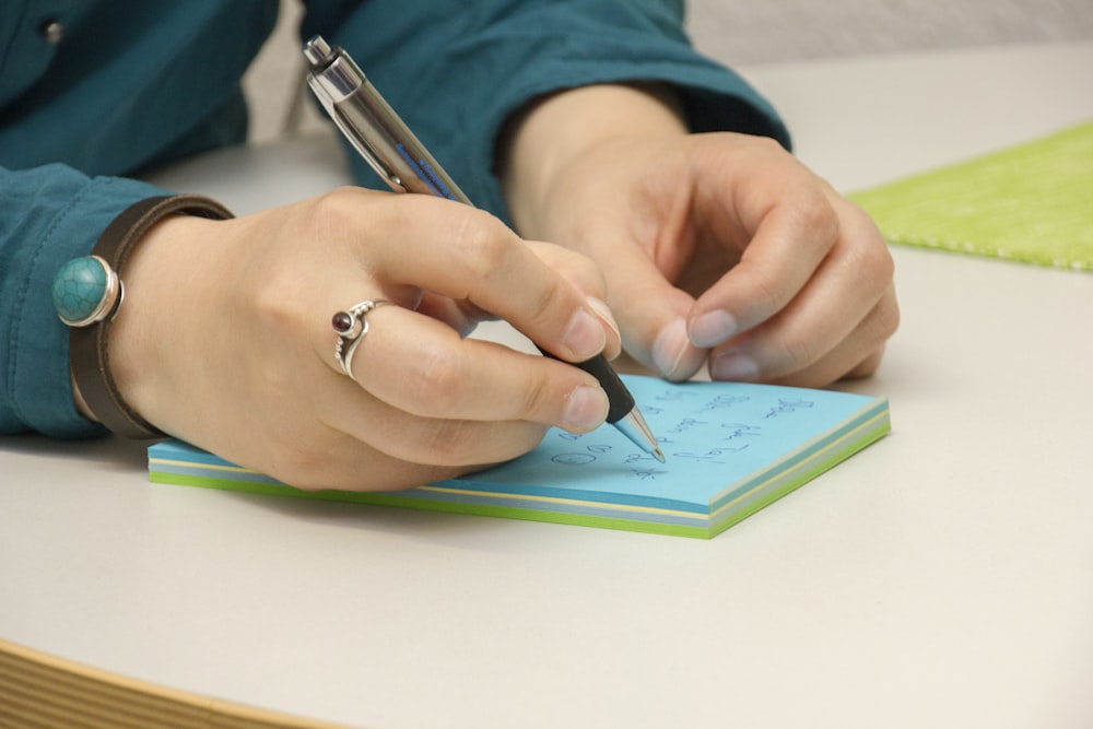 una persona che scrive su un blocco note con una penna