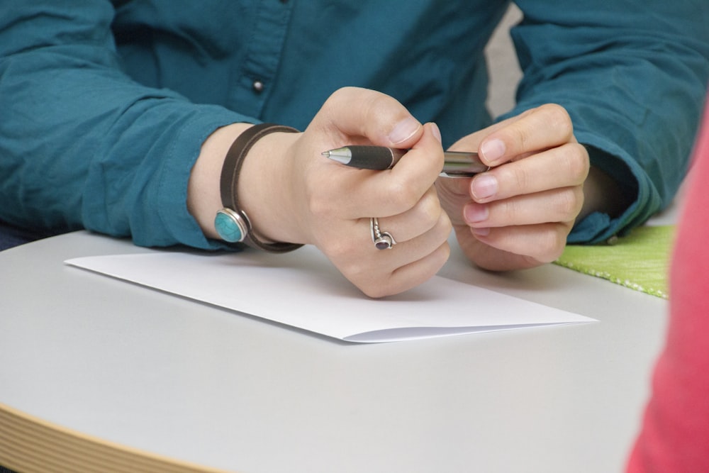 une personne assise à une table écrivant sur un morceau de papier