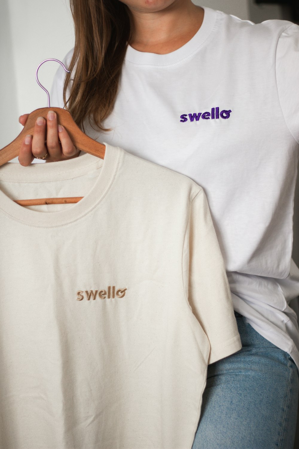 Una mujer sosteniendo una camiseta blanca con la palabra Swelllo