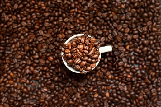 a cup filled with coffee beans sitting on top of a pile of coffee beans