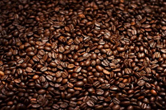 Close-up of glossy coffee beans with golden light reflections on a matte black surface