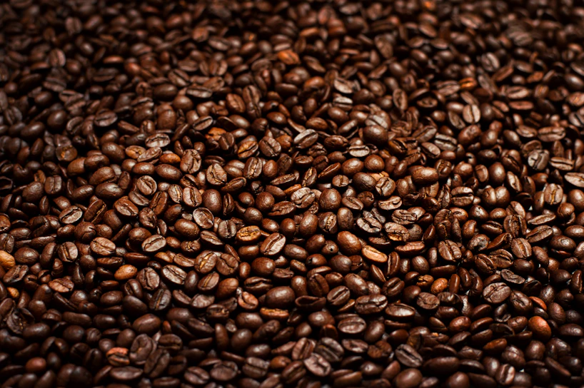 Close-up of glossy coffee beans with golden light reflections on a matte black surface