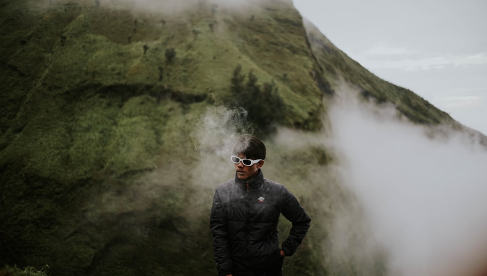 a man wearing sunglasses standing in front of a mountain