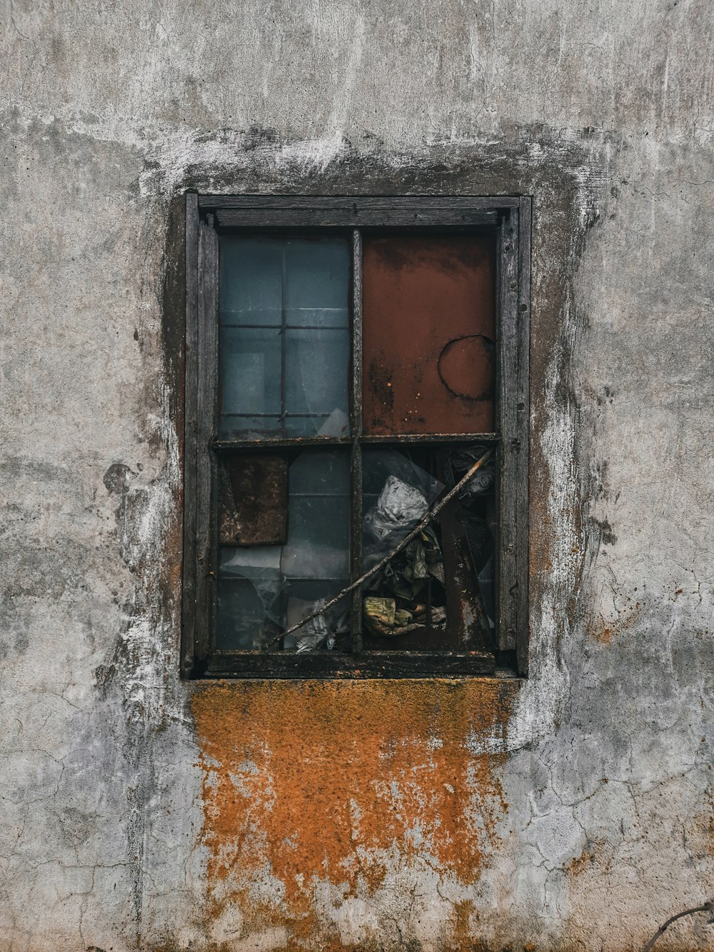 a window with a rusted metal frame on a concrete wall