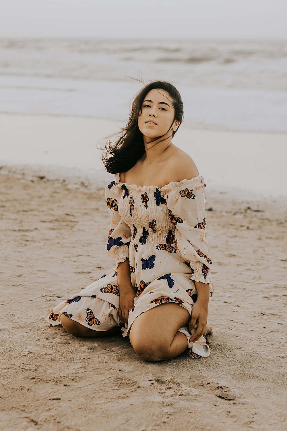 a woman sitting on the beach in a dress