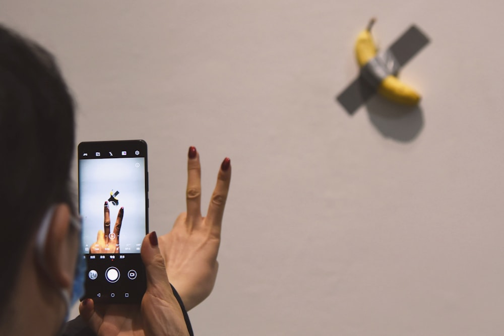 a woman taking a picture of a banana hanging on a wall