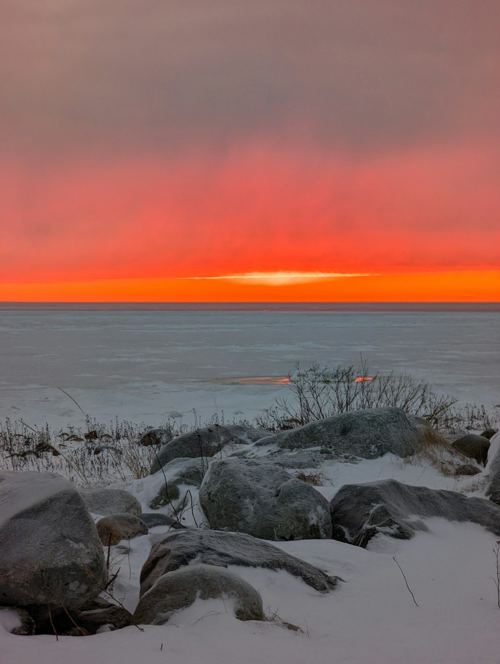 a sunset over a body of water with rocks in the foreground