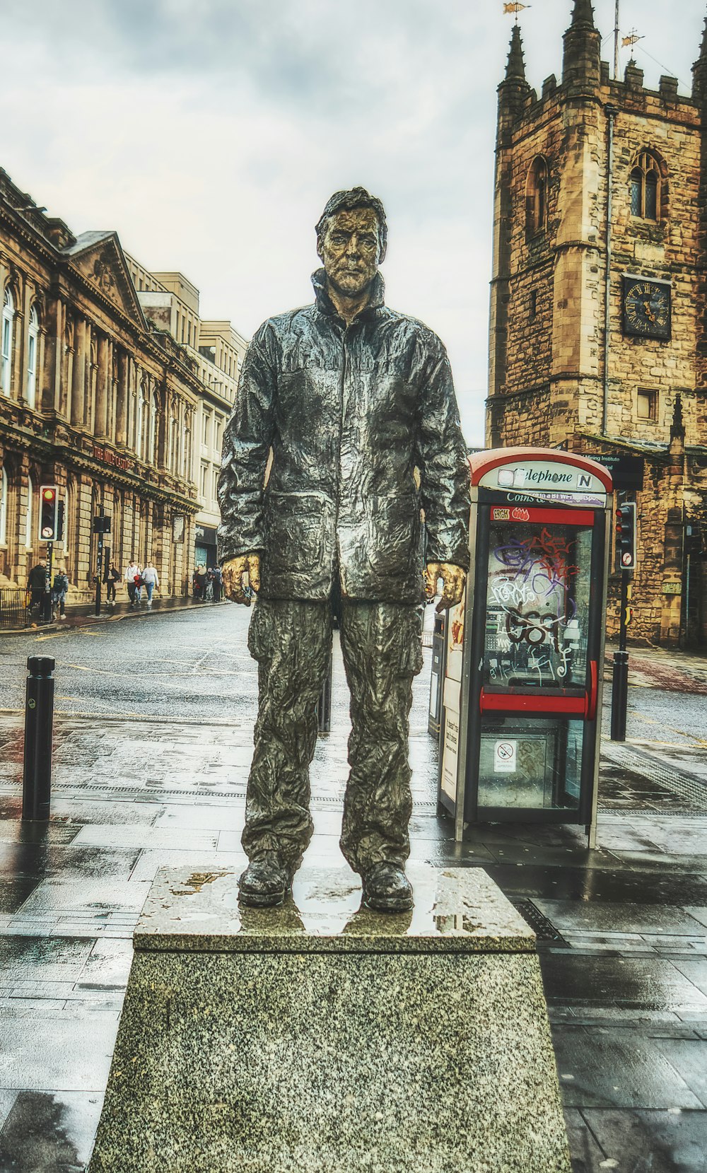 uma estátua de um homem de pé ao lado de uma cabine telefônica