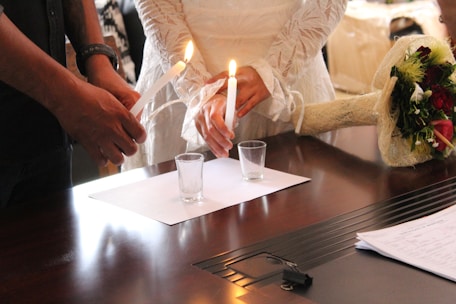 a couple of people that are standing in front of a table lighting candles