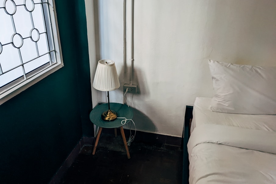 a small table with a lamp on it next to a bed
