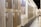 A showroom displaying various wooden flooring samples mounted on walls. A person is observing the samples on the right side, wearing casual attire. The samples are labeled with prices and descriptions. The room is well-lit with a modern design and uses neutral tones.