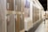 A showroom displaying various wooden flooring samples mounted on walls. A person is observing the samples on the right side, wearing casual attire. The samples are labeled with prices and descriptions. The room is well-lit with a modern design and uses neutral tones.