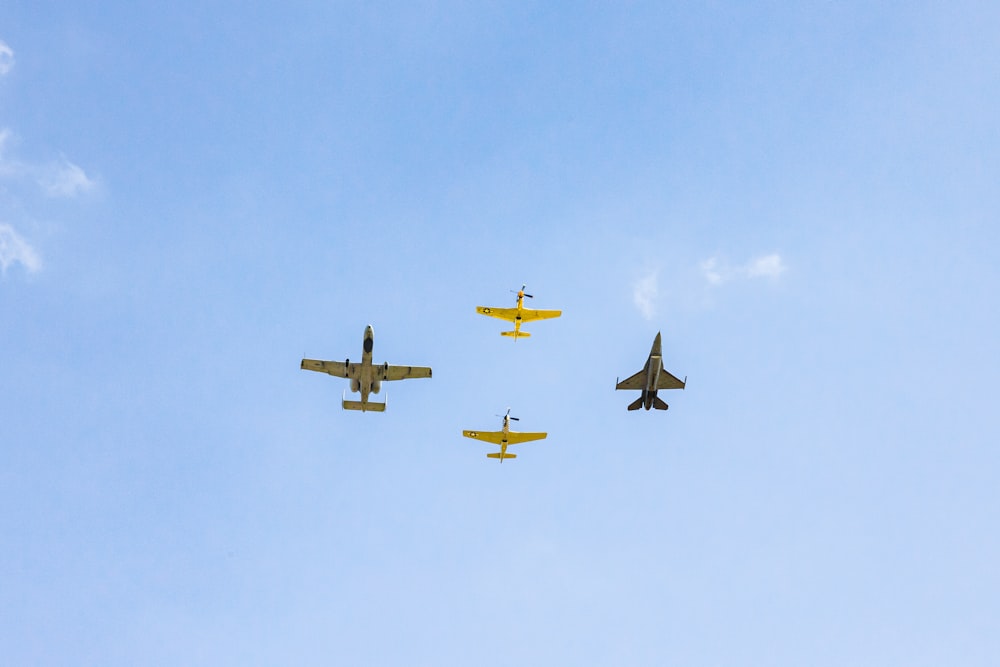 a group of four planes flying through a blue sky