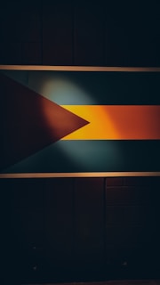 A flag is prominently displayed against a dark background. The flag features a black triangle on the left, followed by a wider horizontal middle section in aquamarine, and a golden-yellow section on the right.