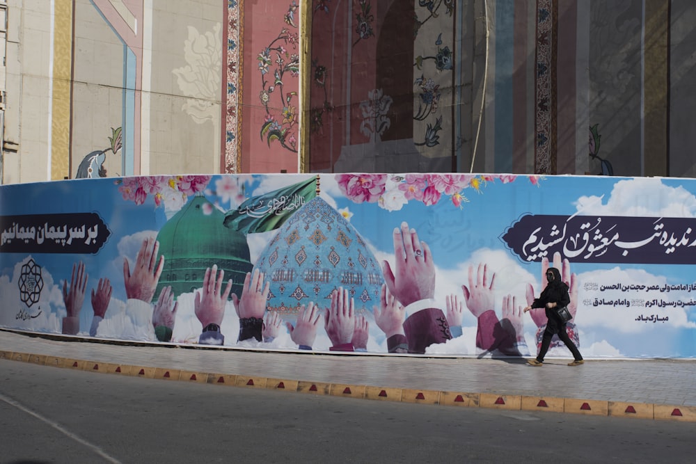 a woman walking down a street past a large mural