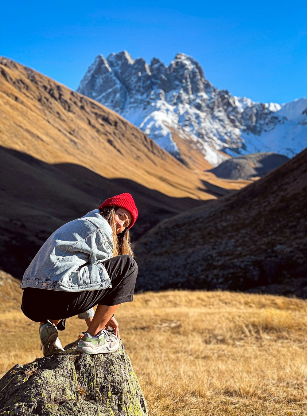 a woman sitting on top of a rock next to a mountain