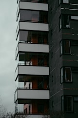 A modern multi-story building with a dark facade and large glass balconies, featuring clean lines and a minimalist design aesthetic.