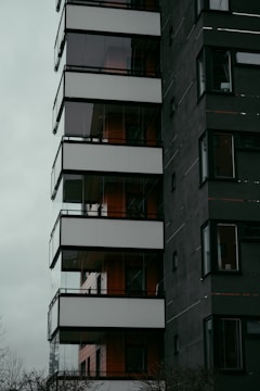 A modern multi-story building with a dark facade and large glass balconies, featuring clean lines and a minimalist design aesthetic.