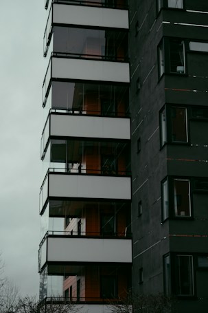A modern multi-story building with a dark facade and large glass balconies, featuring clean lines and a minimalist design aesthetic.