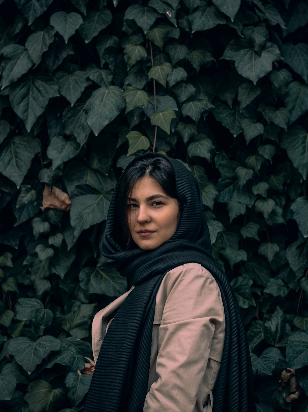 a woman standing in front of a wall of leaves