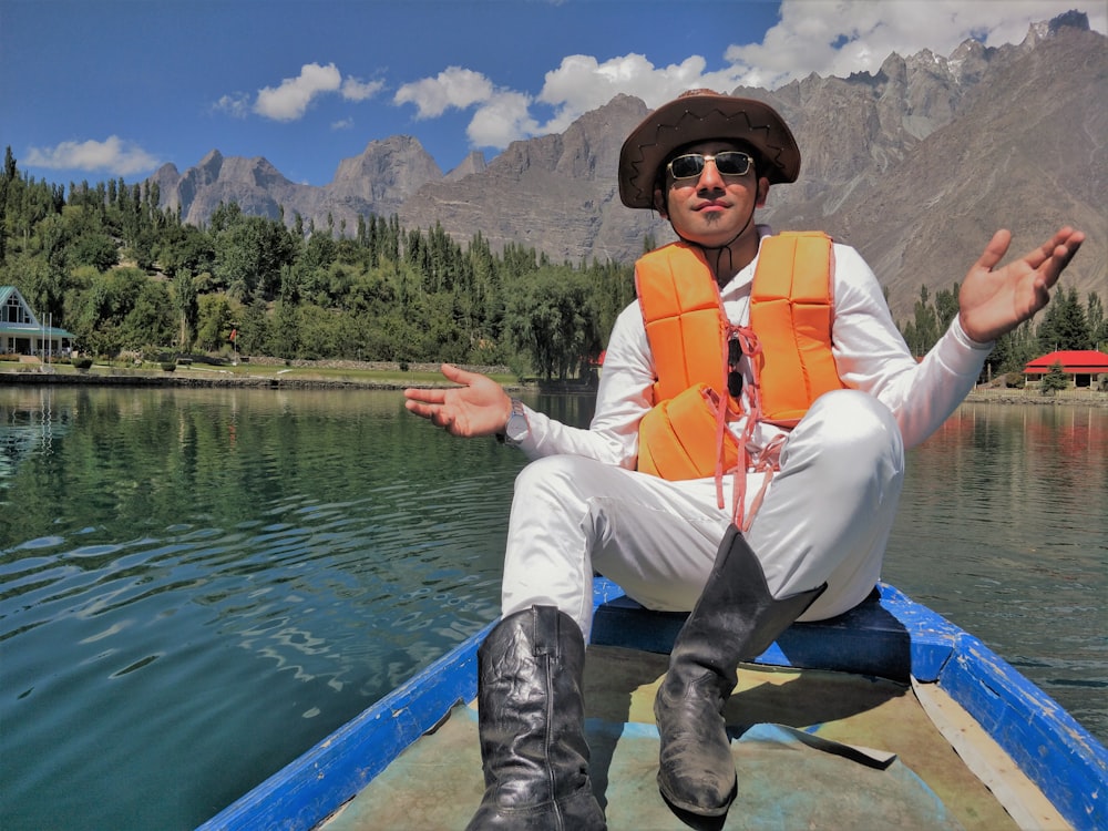 um homem sentado em um barco em um lago com montanhas ao fundo