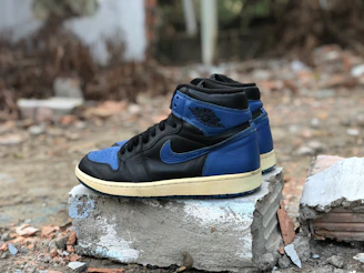Stylish streetwear sneakers in black and blue tones, positioned on a concrete city sidewalk.