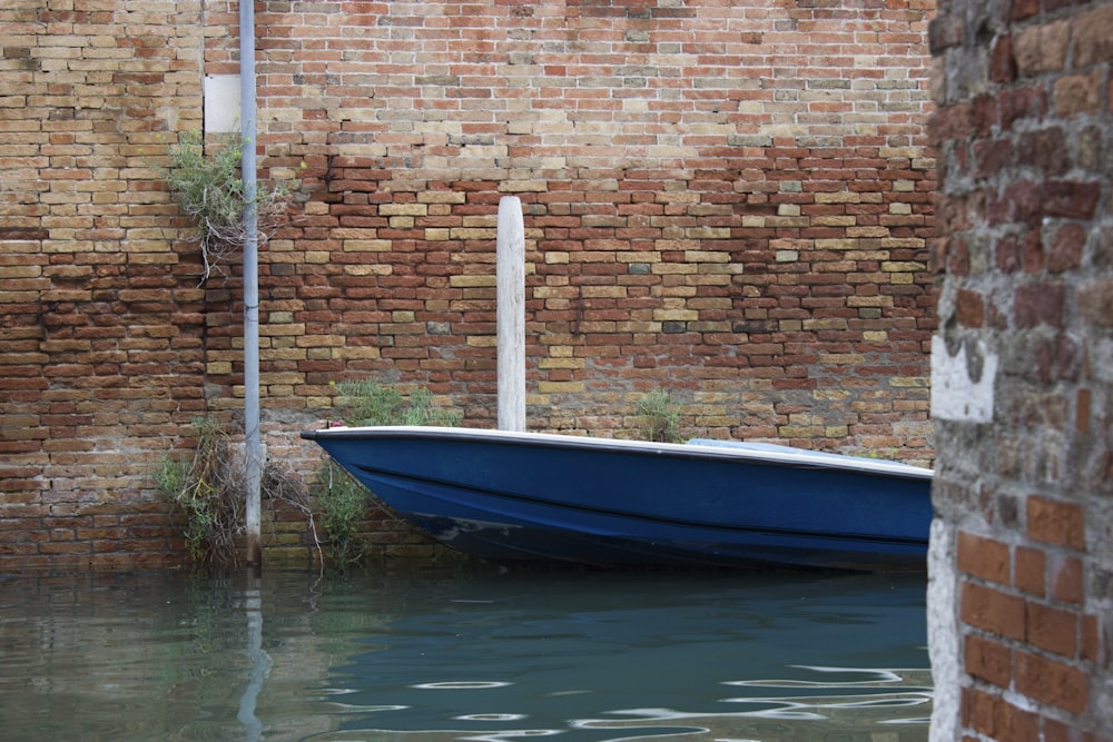 a blue boat sitting in the water next to a brick wall