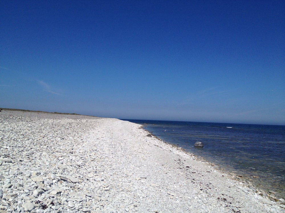 a sandy beach next to the ocean under a blue sky