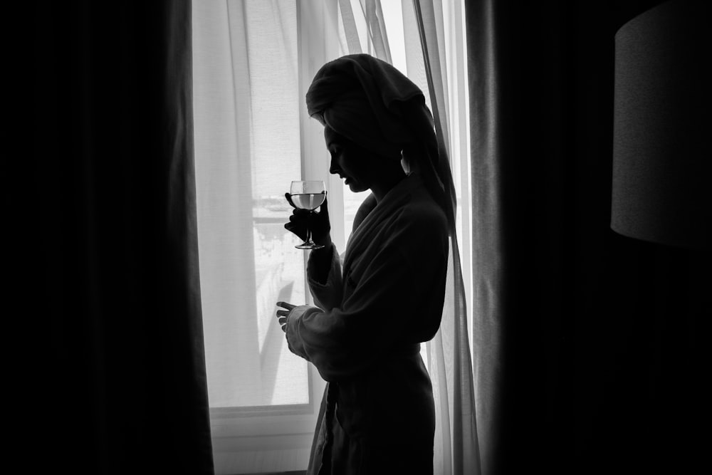 Una mujer parada frente a una ventana sosteniendo una copa de vino