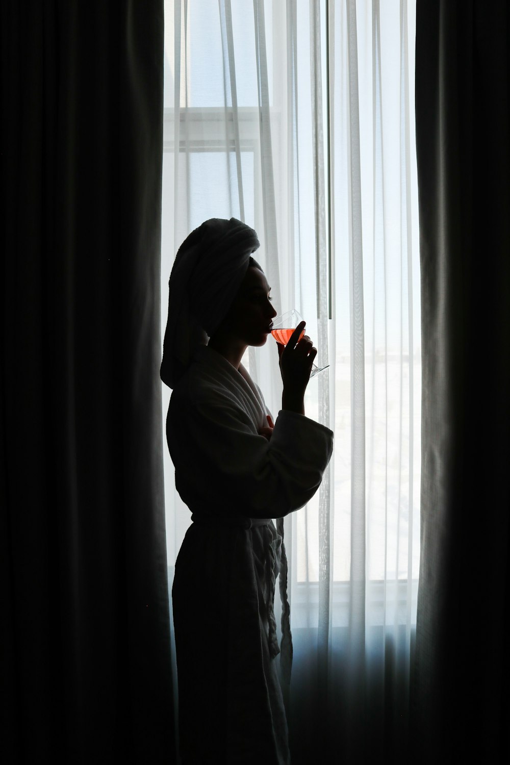 a woman standing in front of a window drinking a glass of wine