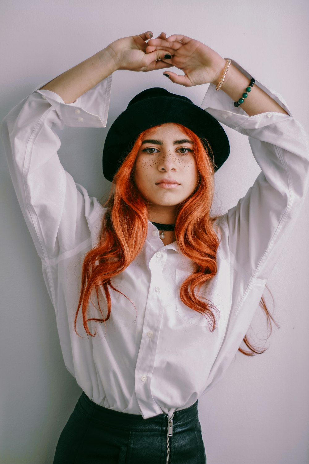 a woman with red hair wearing a white shirt and black hat