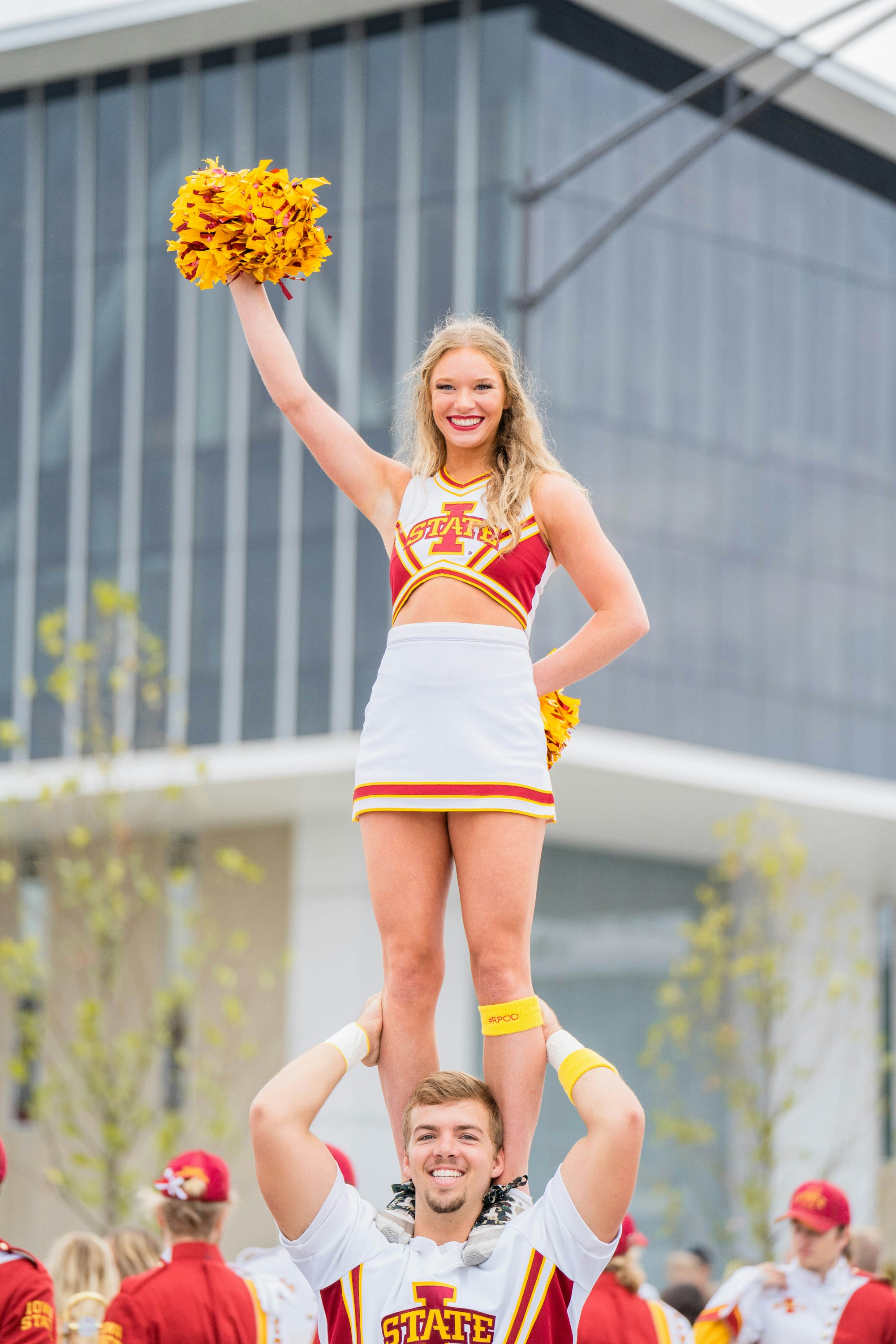 Iowa State University cheerleader cheers with another cheerleader on their shoulders before a football game. 