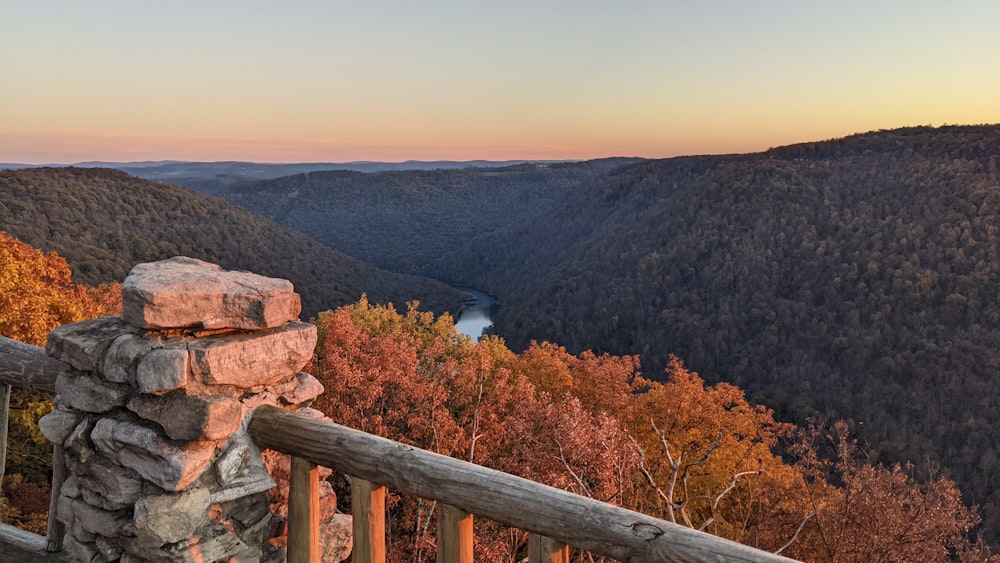 a wooden railing overlooks a valley with a river in the distance