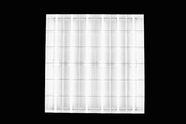 A grid-like pattern composed of translucent glass or acrylic panels, reflecting light and creating a sense of symmetry. The panels are arranged in rows and columns, with subtle shadows and reflections visible.