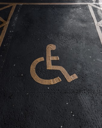A yellow wheelchair symbol painted on a dark asphalt parking space.