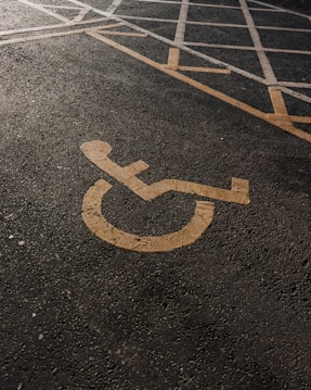 A parking lot is marked with a yellow wheelchair accessibility symbol painted on the asphalt. White lines create boundaries and designate parking spaces.