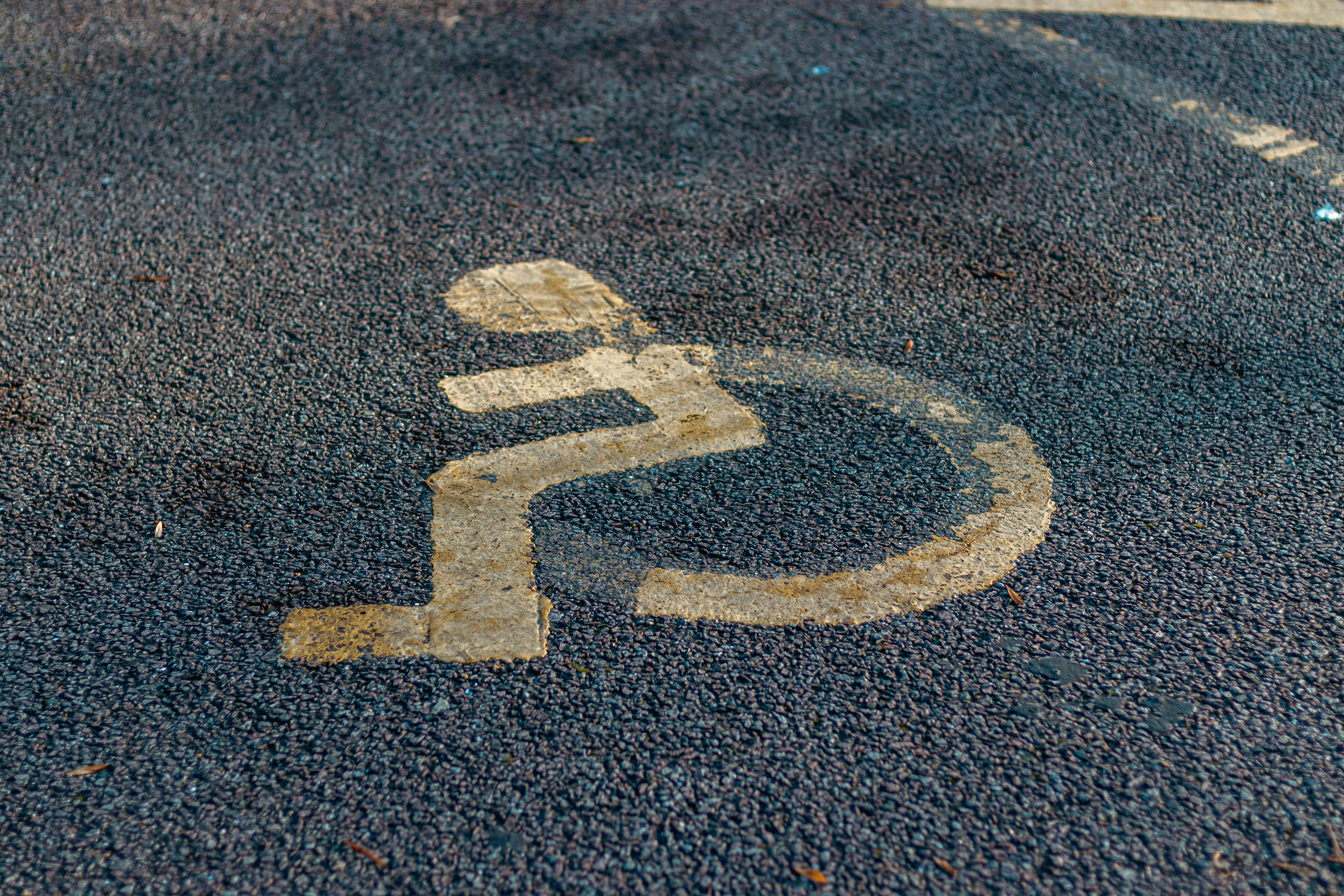 a handicap sign painted on the asphalt of a parking lot, Disabled parking. Accessible parking spot. Blue badge. Yellow wheelchair sign on the ground