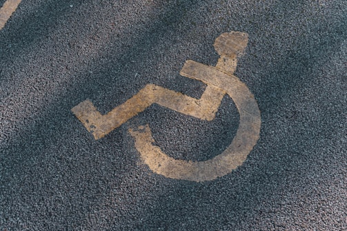 A faded yellow wheelchair symbol is painted on a textured asphalt surface, often seen in parking areas reserved for individuals with disabilities.