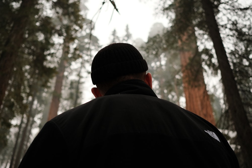 a man in a black jacket standing in a forest