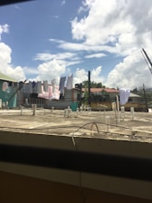 A rooftop with several clothes hanging on lines to dry under a bright blue sky with scattered clouds. The scene includes some urban residential buildings in the background.