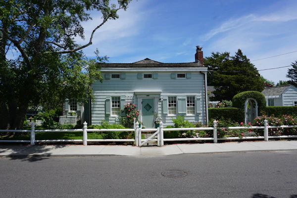 A heritage shingle-style home with white picket fencing under soft afternoon light on the East End