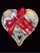 A heart-shaped basket filled with an assortment of cookies, adorned with a red ribbon tied into a bow. The cookies vary in style, featuring jam-filled centers, powdered sugar coatings, and chocolate drizzles.