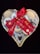 A heart-shaped basket filled with an assortment of cookies, adorned with a red ribbon tied into a bow. The cookies vary in style, featuring jam-filled centers, powdered sugar coatings, and chocolate drizzles.
