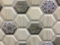 Hexagonal tiles are arranged in a repeating pattern, with some tiles featuring intricate blue and white floral designs. The surrounding tiles have a more subdued, stone-like appearance in various shades of gray.