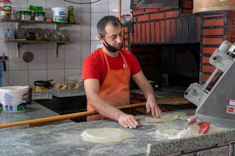 a man in an orange shirt making pizzas in a kitchen