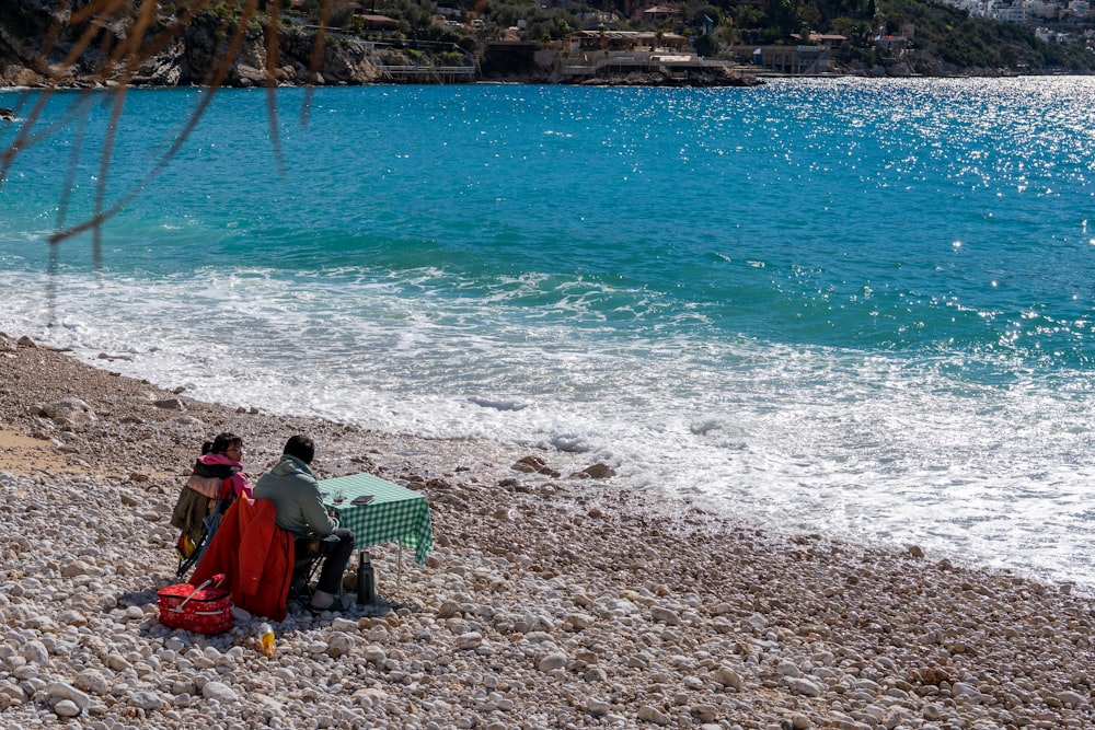 a couple of people sitting on top of a sandy beach