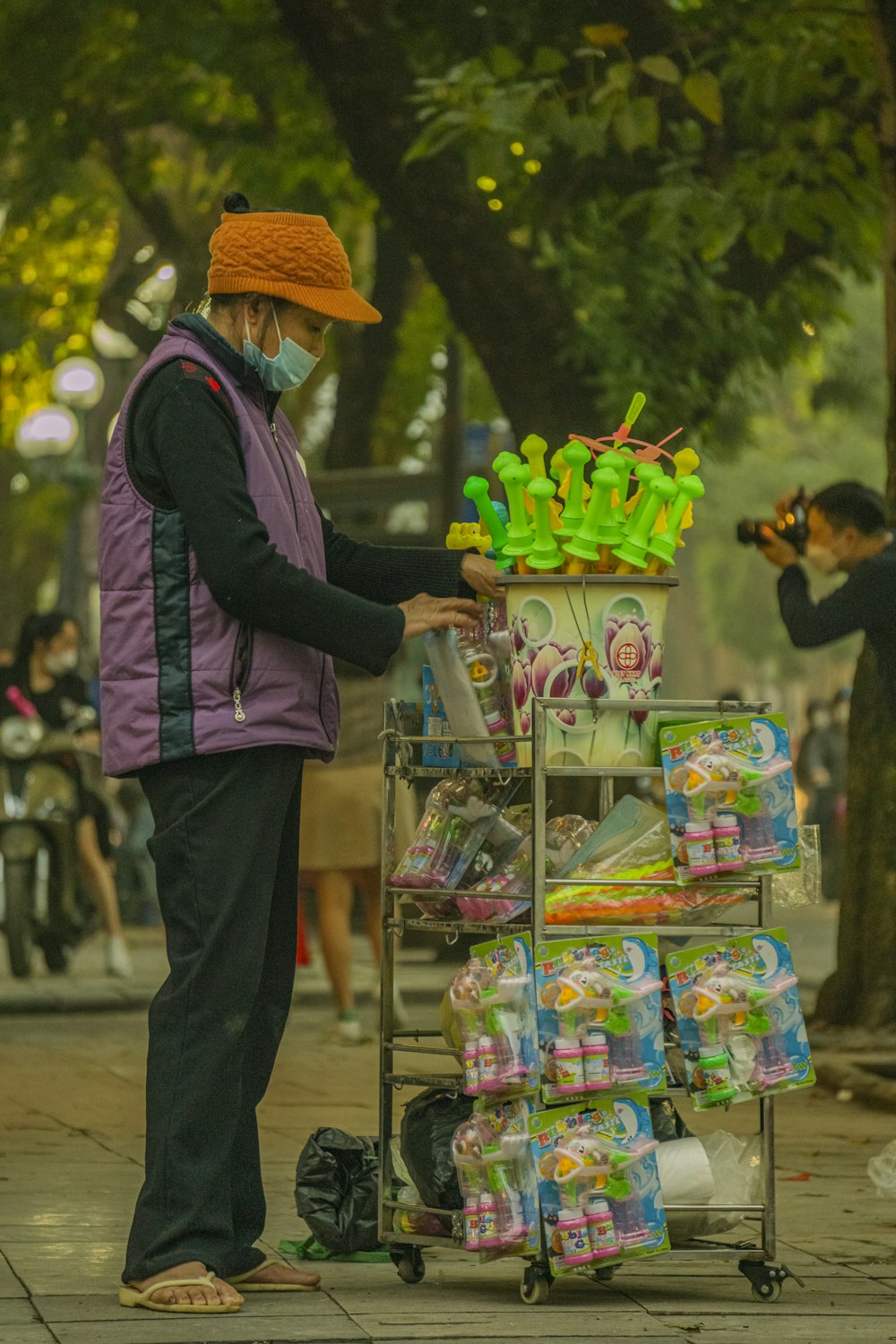 um homem em um colete roxo e chapéu laranja está empurrando um carrinho cheio de itens